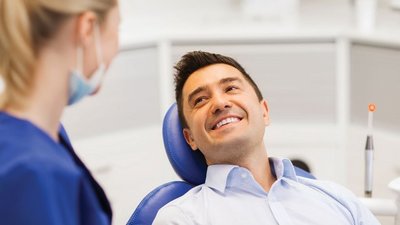 Photo of young man in dental chair chatting with dental professional